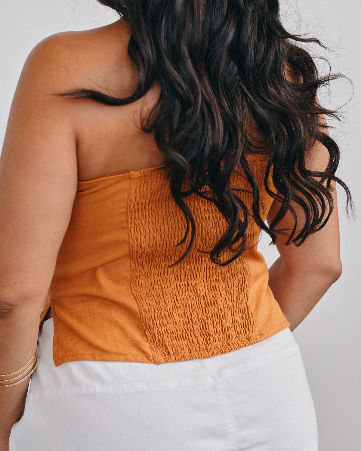 Woman wearing a smocked orange top with white pants against a neutral background
