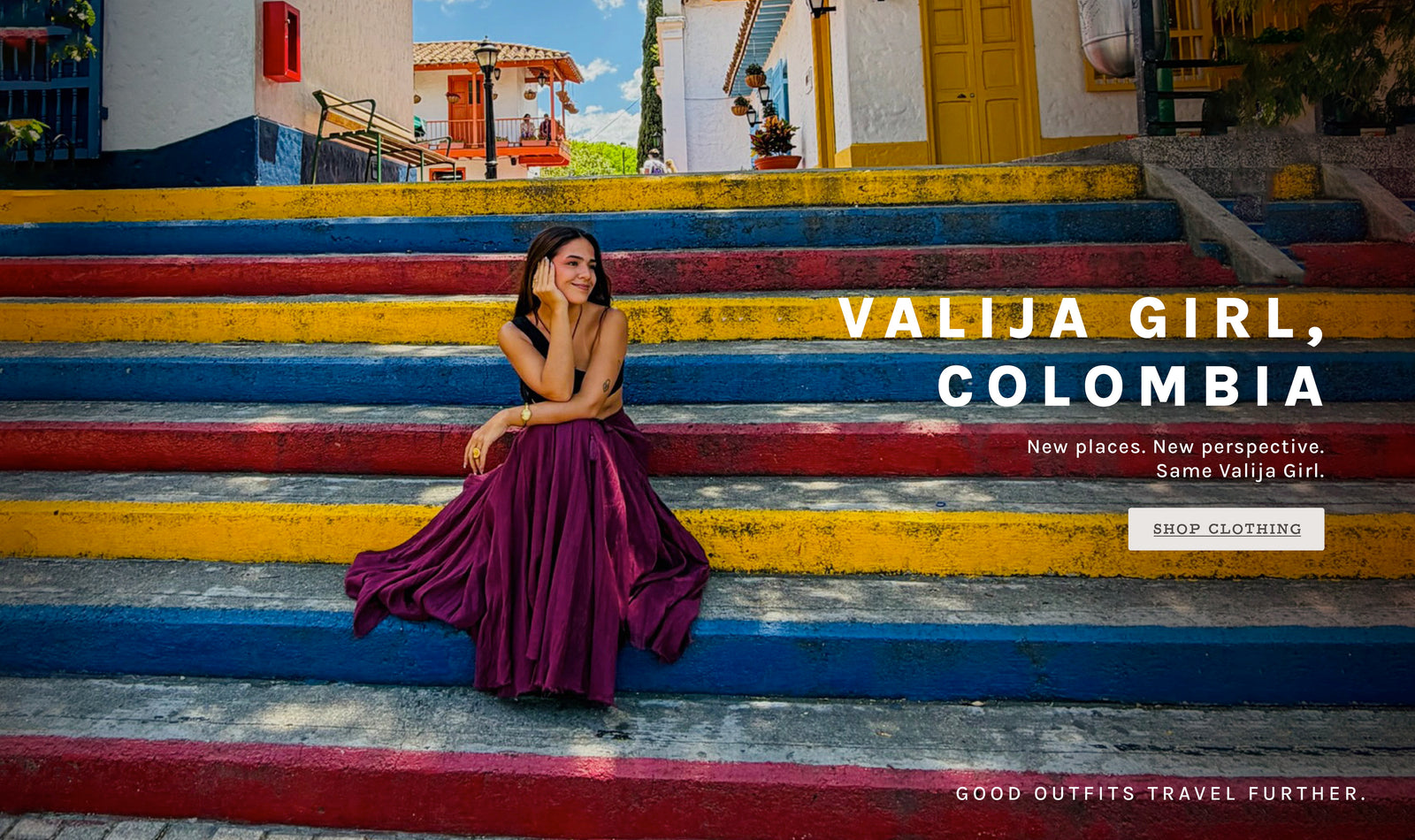A woman in a flowing dark purple maxi dress sits on colorful painted steps in front of a building in Colombia. Text on the image reads 'VALIJA GIRL, COLOMBIA' with a 'SHOP CLOTHING' button.