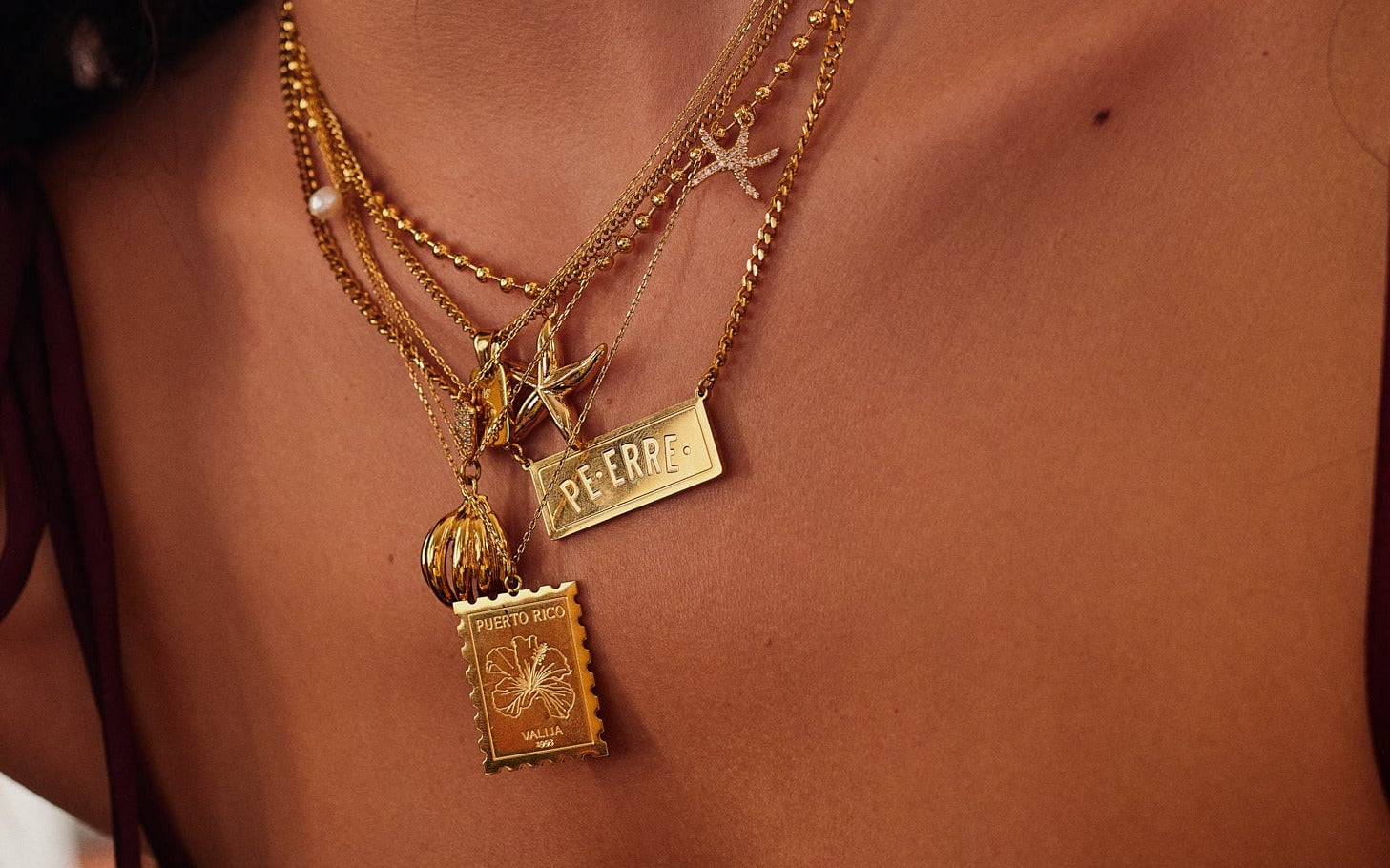Close-up of a person wearing multiple gold necklaces with star and postage-stamp pendants.