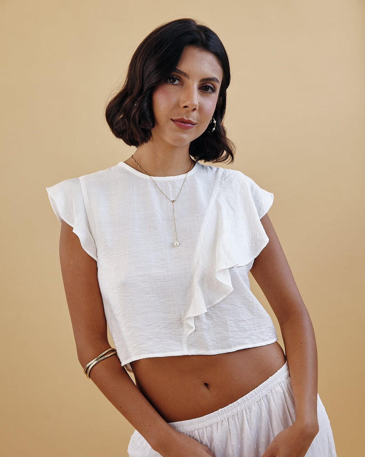 Woman wearing a white top and skirt against a beige background