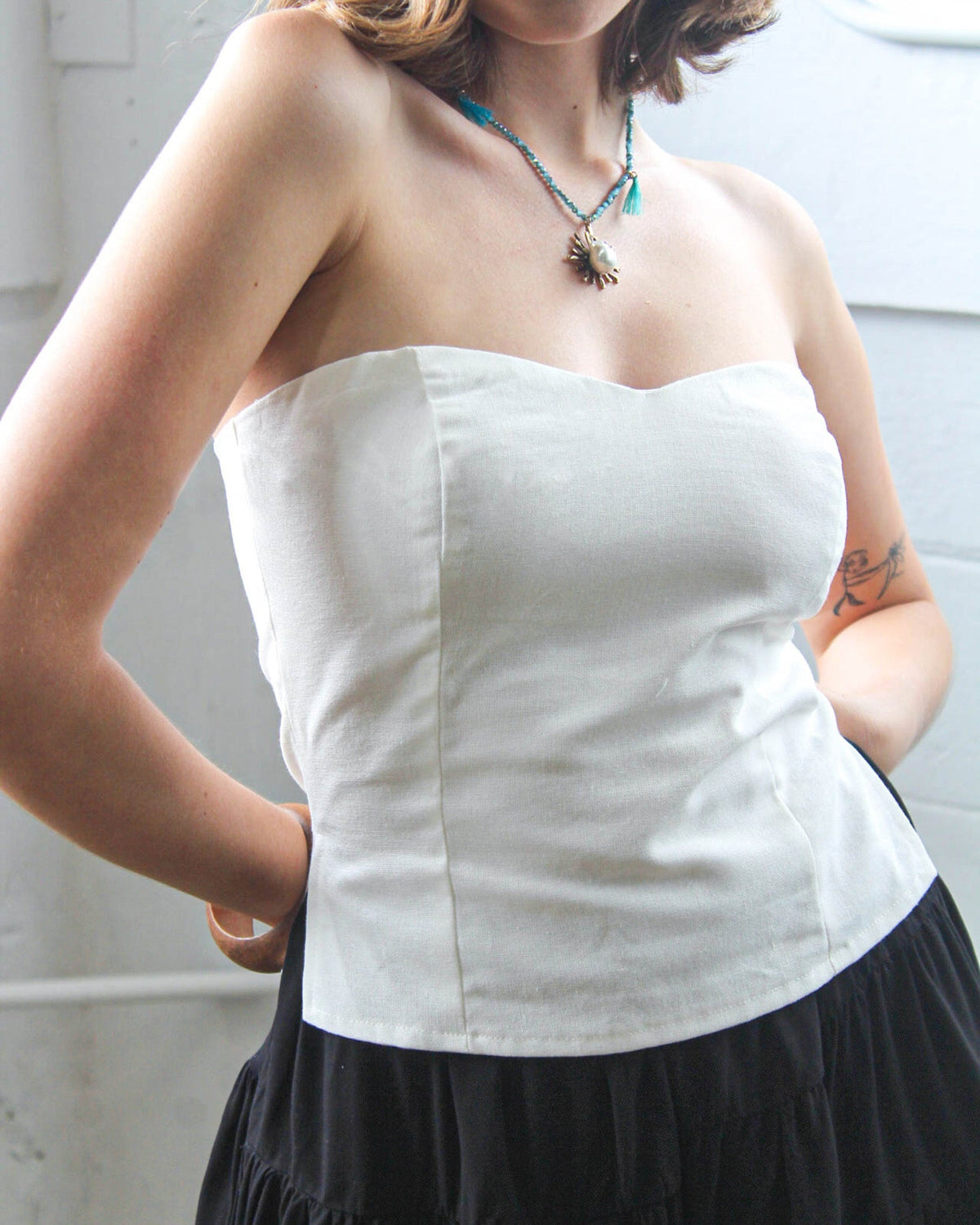 Person wearing a strapless white top and black skirt with a neutral background